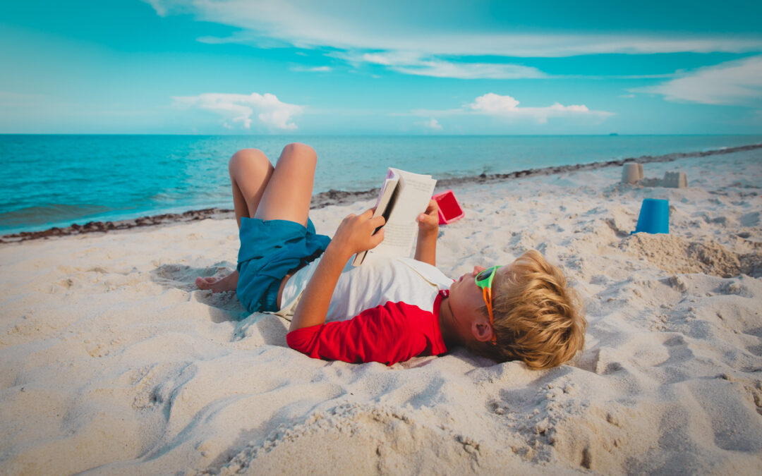 Child reads at beach, showing how learning can happen during vacation.